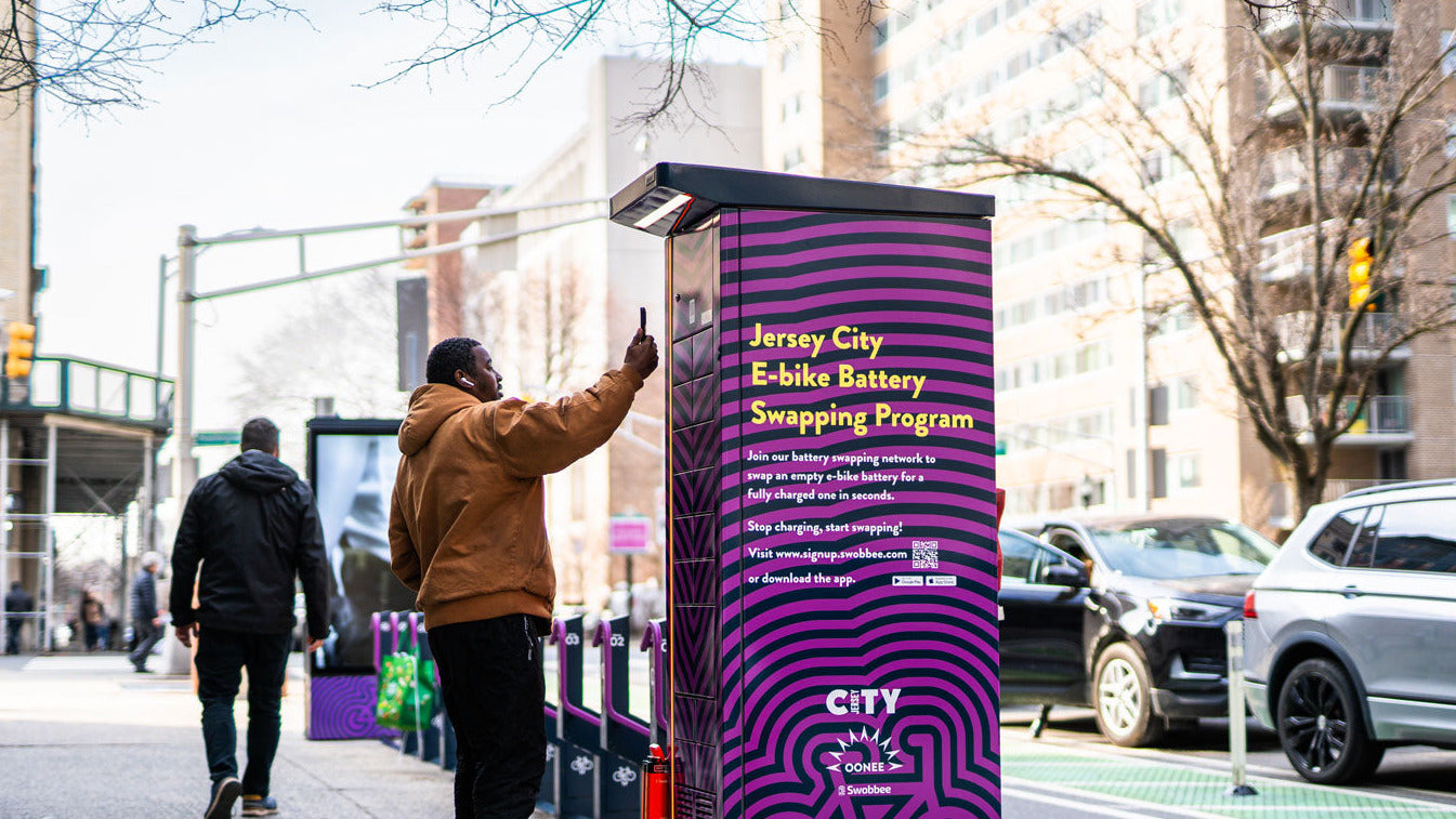 Person interacting with a Jersey City e-bike battery swapping program station on a city street.